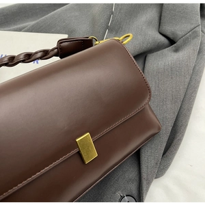 Detail of a brown leather handbag featuring a woven handle and gold square clasp