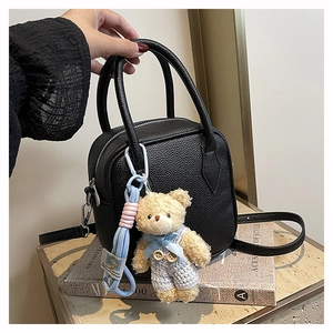 Detail of black pebbled leather square bag with plush bear charm and striped cord accessory