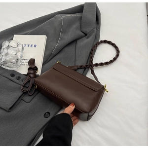 Detail of dark brown leather crossbody bag with woven strap and gold hardware on blazer