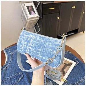 Detail of light blue woven pillow bag featuring flower charm and metal chain strap