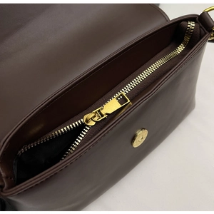 Detail of dark brown leather crossbody bag featuring a golden zipper and magnetic closure