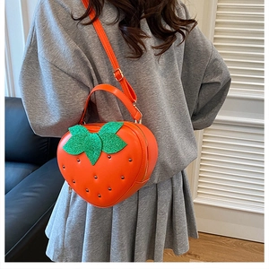 Détail d'un sac à bandoulière orange en forme de fraise avec feuille verte à paillettes