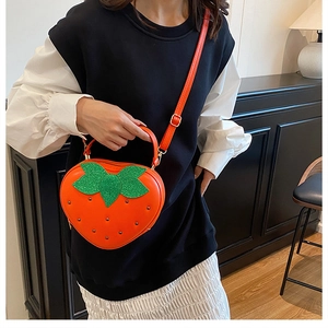 Détail du sac bandoulière orange en forme de fraise avec feuilles en paillettes et rivets