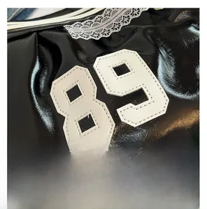 Macro detail of glossy black bag showing white number 89 patch with white lace trim details