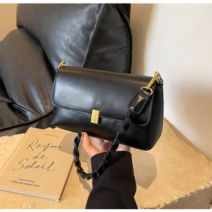 Detail of minimalist black leather shoulder bag with gold square buckle and chunky chain