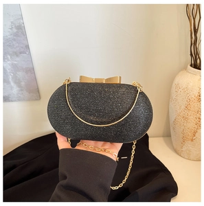 Close-up of black glitter evening clutch with gold bow clasp and metal chain strap