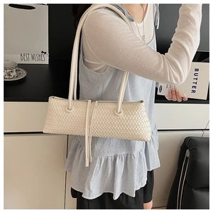 Detail of a minimalist off-white woven shoulder bag shown on a model in a modern room