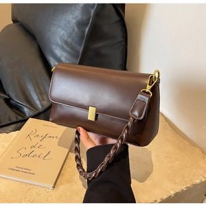 Detail of dark brown leather underarm bag with gold buckle and woven strap on stone surface
