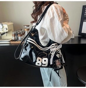 Detail of black glossy PU leather tote bag with number 89 patch and white stripe accents