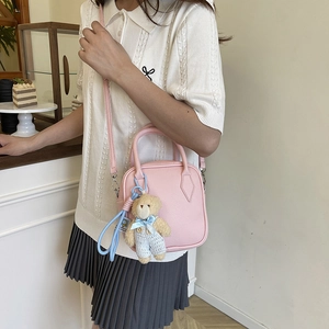 Pink lychee grain crossbody mini bag with teddy bear charm on a coffee shop background