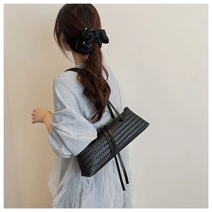 Détail d'un sac à bandoulière noir en cuir tressé porté par un mannequin sur fond épuré