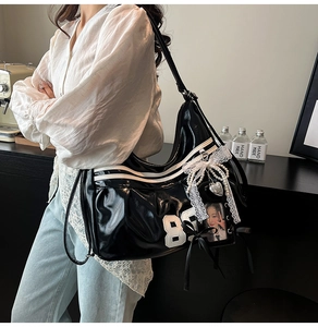 Detail of black glossy baseball style tote bag with white trim and lace heart charms