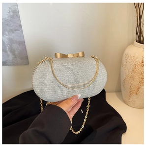Close-up of silver glitter evening clutch bag with bow clasp and gold chain strap