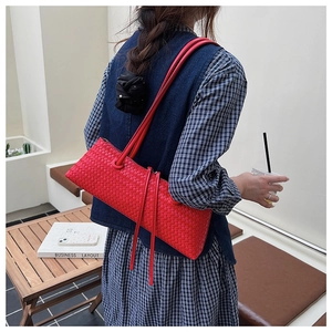 Détail d'un sac baguette tressé rouge vif avec pompon à franges et doubles lanières