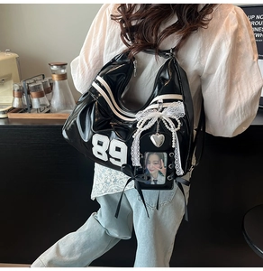 Detail of glossy black faux leather crossbody bag with 89 embroidery and lace bow charm