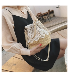 Detail showing the white floral lace stitching on a woven straw bucket bag with drawstrings