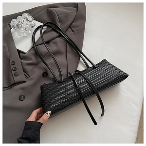 Macro view of woven leather texture on a black minimalist baguette underarm shoulder bag