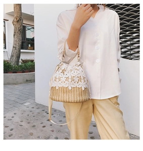 Detail of woven straw bucket bag featuring delicate white lace trim and leather straps