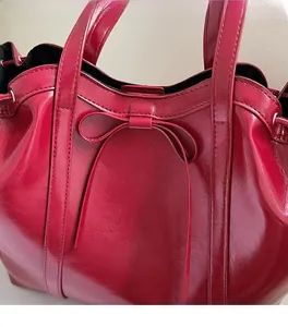 Detail of red glossy patent leather tote bag with a small decorative bow and handles