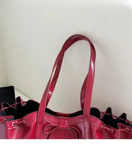 Detail of red patent leather tote bag featuring drawstring closure and decorative bow knot