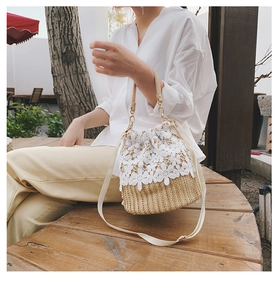 Detail of straw bucket bag with white lace floral appliques and drawstring closure