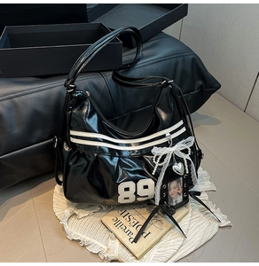 Detail of black patent leather hobo bag featuring white number 89 and aesthetic charms