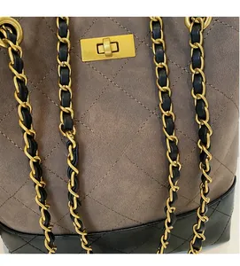 Close-up of quilted suede shoulder bag with gold chain strap and metallic lock detail