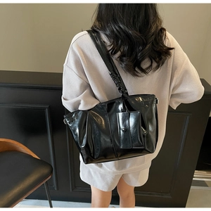 Dettaglio della borsa tote nera lucida con pochette indossata sulla spalla della modella