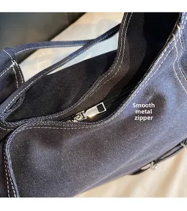 Detail view of silver metal zipper and white stitching on dark blue denim bag