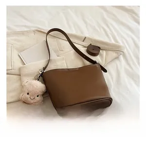 Detailed view of a brown bucket bag with a cute plush toast charm and spare strap