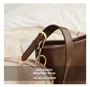 Detail of adjustable brown leather strap with gold buckle and plush charm on bucket bag