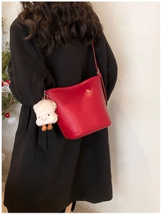 Red leather bucket bag with white sheep pendant shown on a model in a black coat