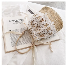 Close-up of woven straw bucket bag featuring white lace flowers and gold hardware accents