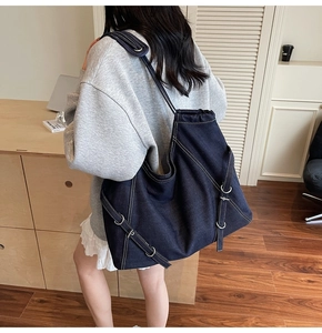 Detail of dark blue denim tote bag featuring white contrast stitching and buckle straps