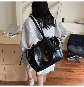 Detailed view of black faux leather tote featuring bow decoration and drawstring closure