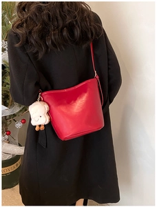 Detail of red leather bucket bag with a white plush lamb charm on a shoulder strap