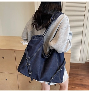Detail of large navy denim tote bag with white contrast stitching and metallic ring accents