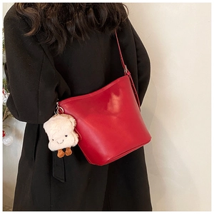 Detail of red bucket shoulder bag with plush toast pendant and thin strap on a model