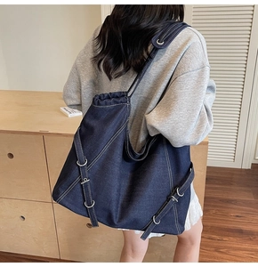 Detailed view of the dark blue denim tote bag with white contrast stitching and silver rings
