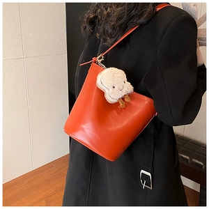 Detail of red leather bucket bag with cute plush toast charm on model in dark interior