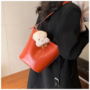 Side view of orange leather bucket bag with a cute plush toast pendant on a black coat