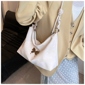 Detail of white half-moon shoulder bag featuring a metallic butterfly buckle and knotted strap