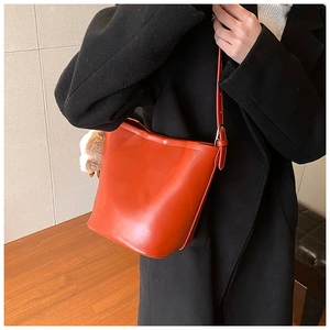Detail of vibrant orange leather bucket bag with adjustable strap worn on black coat