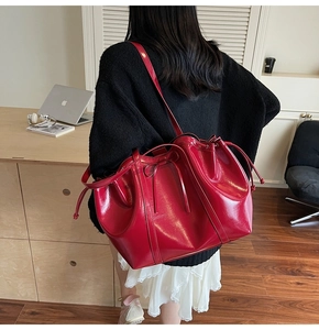 Detailed close-up of a red patent leather tote bag with drawstring and bow detail