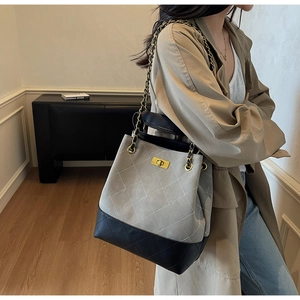 Detail of grey quilted bucket bag with chain strap and black base on a model