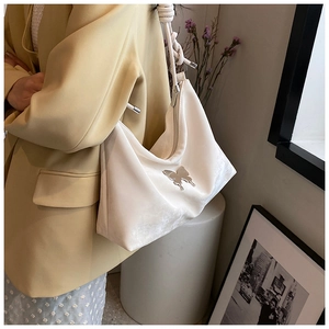 Detail of white velvet tote bag featuring a silver butterfly charm and braided rope strap