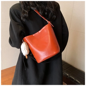 Detail of an orange-brown bucket bag with a plush charm accessory and thin strap