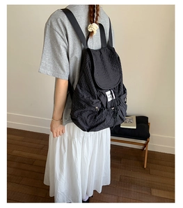 Side view of a black checkered nylon backpack with drawstring and side pockets on a model