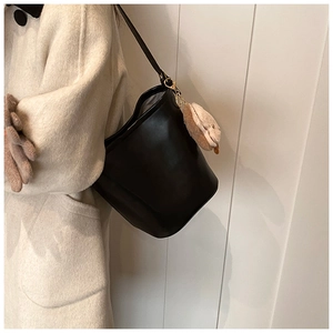 Black leather bucket bag with cute plush animal charm shown on a stylish model coat