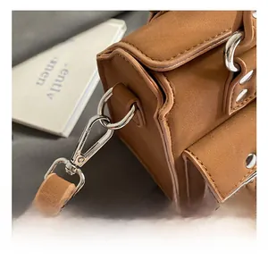 Detail of silver polished metal hook and caramel matte leather strap on shoulder bag